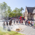 Smoking ceremony on the paved area at Walyalup Koort with St John's Church in the background